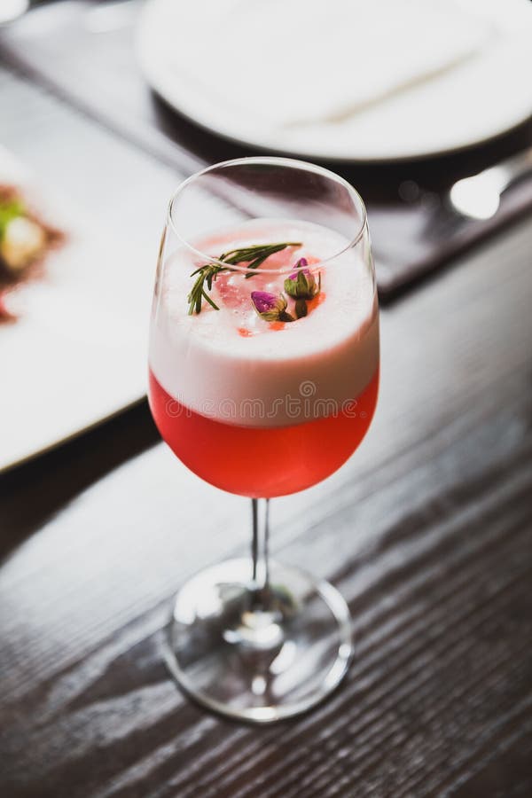 Red Cocktail in Wine Glass Topping with Foam, Flowers and Rosemary