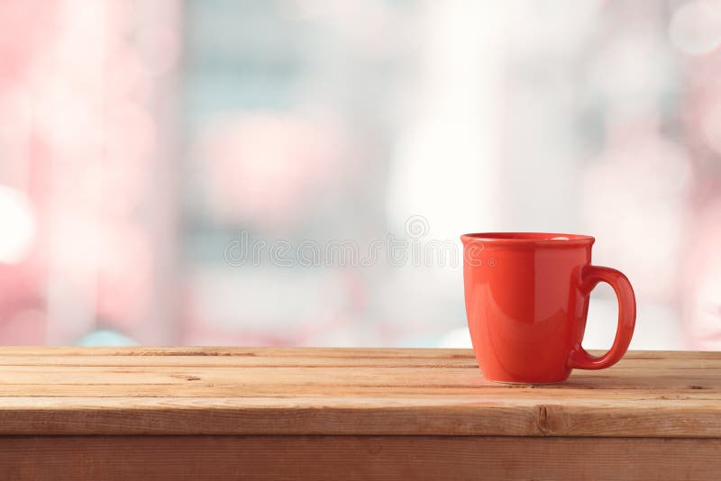 Red coffee or tea cup on wooden table over abstract bokeh background with copy space