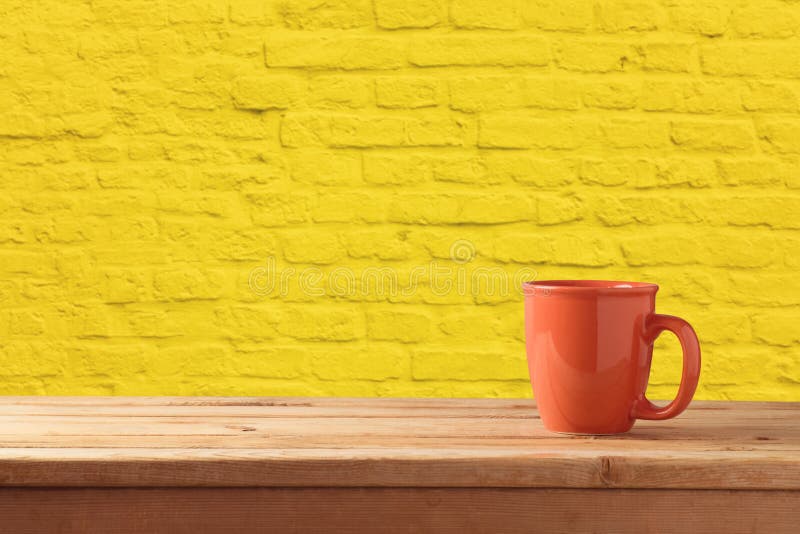 Red coffee or tea cup on wooden table over yellow brick stone wall background