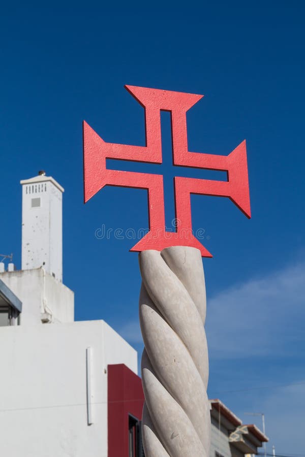 Red cross at church Igreja Matriz de Alvor. Building with a white facade and chimney in the background. Deep blue sky with a wite