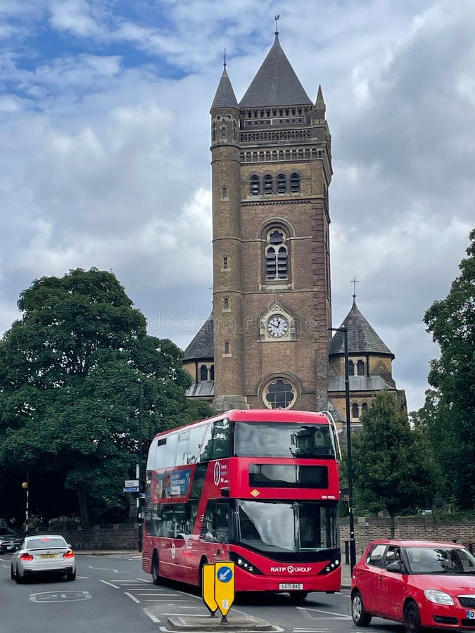 Red double-decker bus in front of a historic church in London on a cloudy day stock images