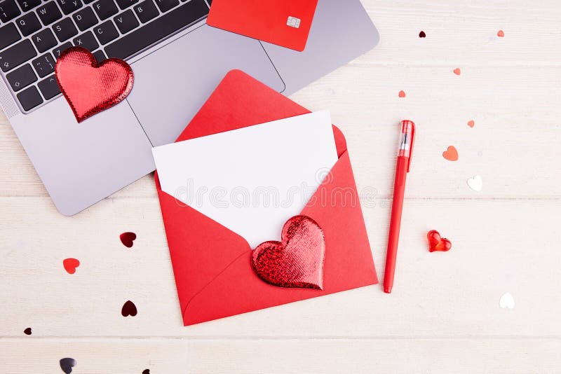 A red envelope with an empty sheet of paper , a pen, a laptop, a credit card, decor, hearts