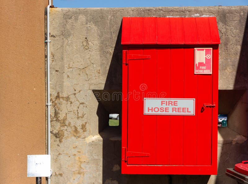 Red Fire Hose Reel, Mounted on Old Concrete Wall Background Stock Photo