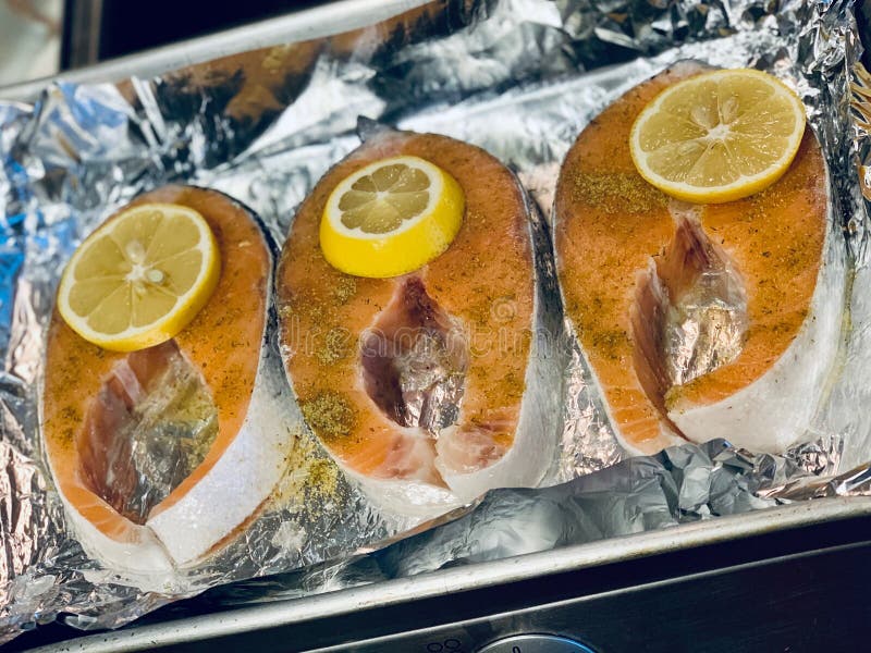 Fish steaks with lemon wedges on foil stock photo