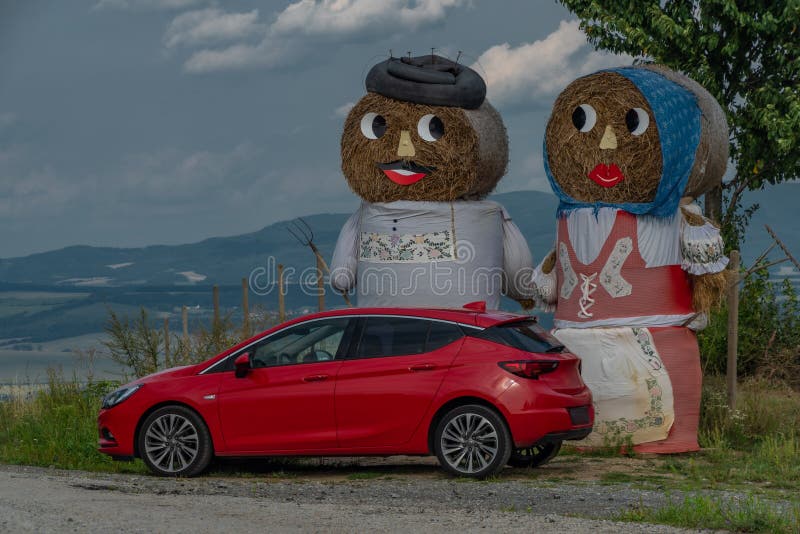 Red fresh car with hay puppets in field in summer hot day