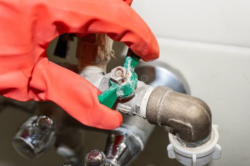 A red-gloved hand turns a green knob on a connecting valve on a chrome-plated faucet, covered with limestone stock photo A red-gloved hand turns a green knob on a connecting valve on a chrome-plated faucet, covered with limestone stock photo