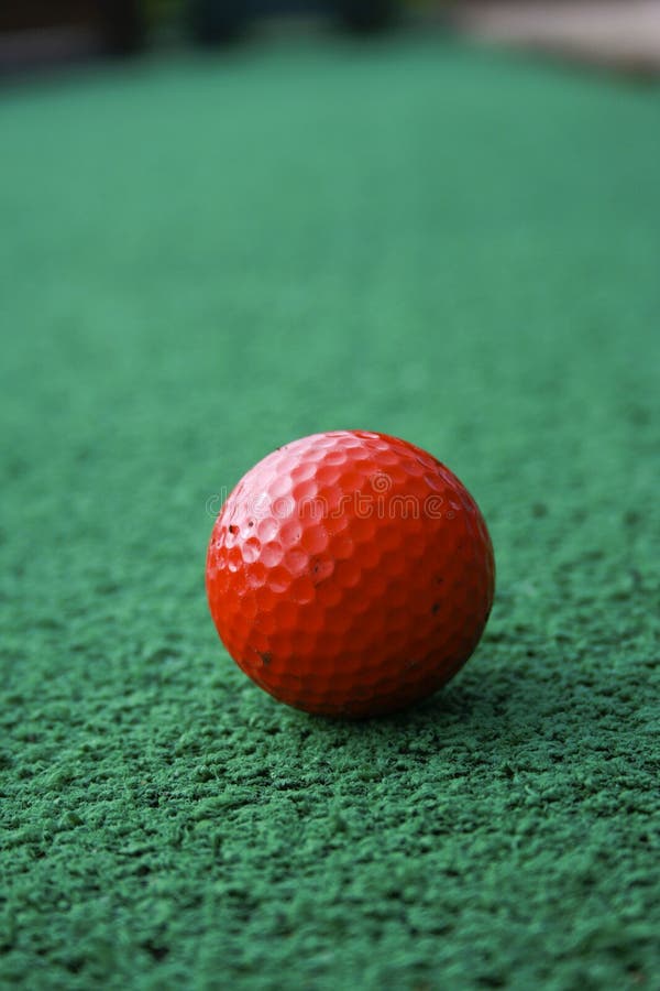 A red golfball sitting on the green of a mini putt course. A red golfball sitting on the green of a mini putt course.