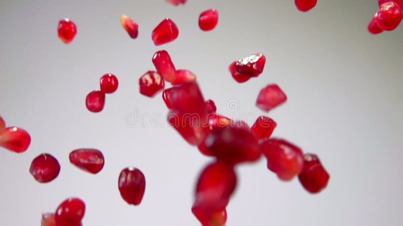 Red grains of ripe pomegranate are flying up down on the white background