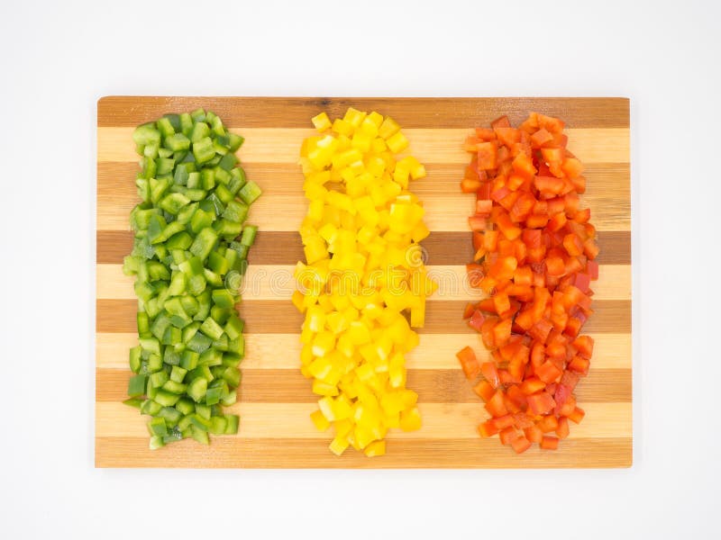 Red, green and yellow sweet bell peppers chopped on a wooden cutting board