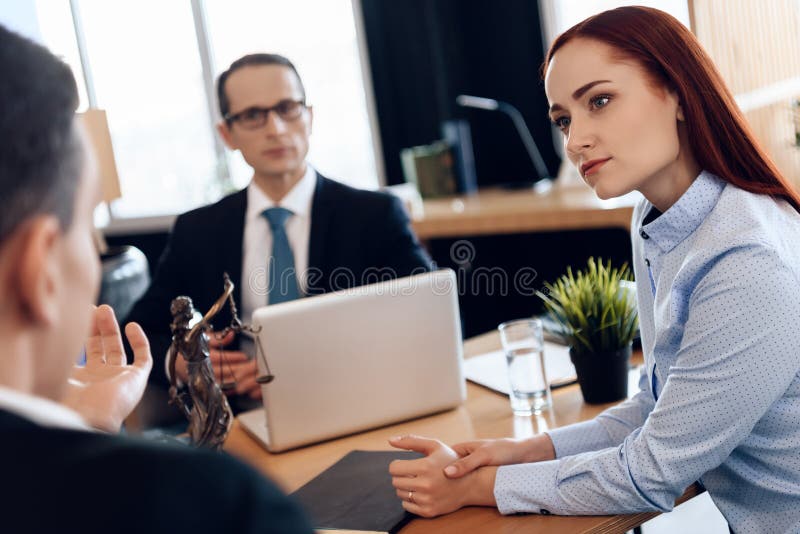 Red-haired beautiful women listens attentively to men looking at divorce attorney. Attorney in business suit is sitting at office table, listening to discussion of divorcing couple. Red-haired beautiful women listens attentively to men looking at divorce attorney. Attorney in business suit is sitting at office table, listening to discussion of divorcing couple.