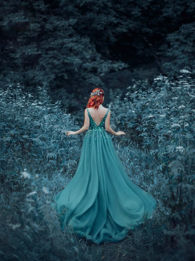 Red-haired girl in a blue, sapphire, luxurious dress in the floor, with an open back and a long train. The princess