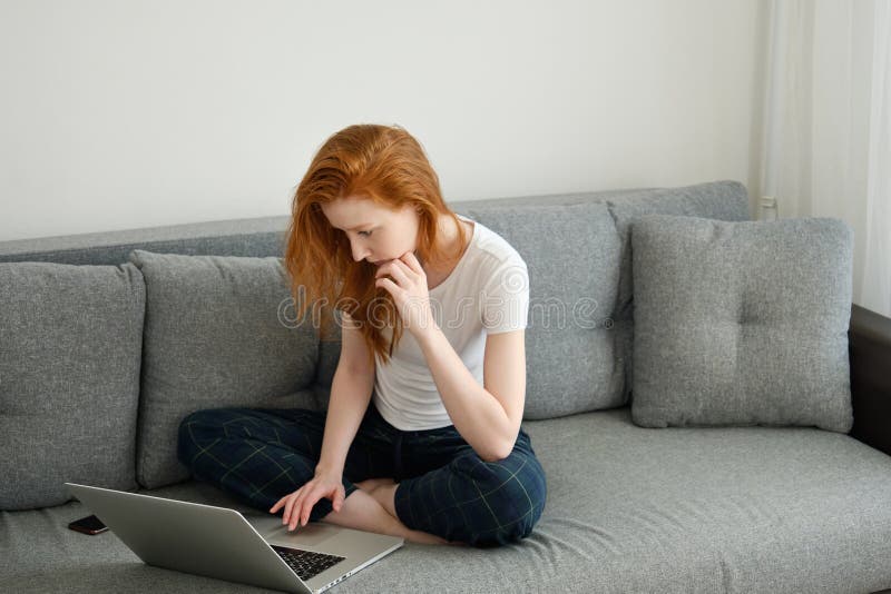 A Red Haired Girl In Home Clothes Sits Half Turn On The Couch Wearily 