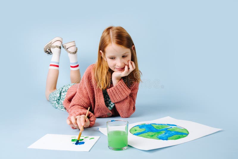 Red-haired girl lying on the floor draws a green-blue planet
