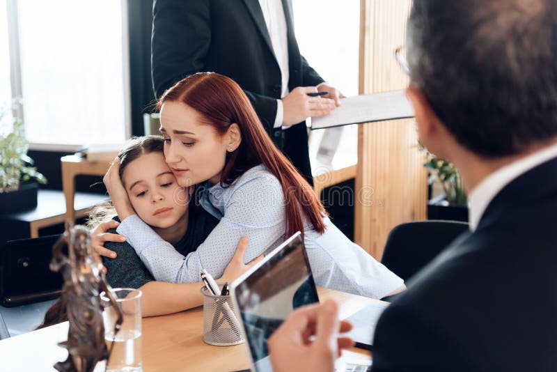 Red-haired sad women hugs little upset girl sitting in lawyer`s office for divorce. Two parents fighting over child in divorce concept. Red-haired sad women hugs little upset girl sitting in lawyer`s office for divorce. Two parents fighting over child in divorce concept.