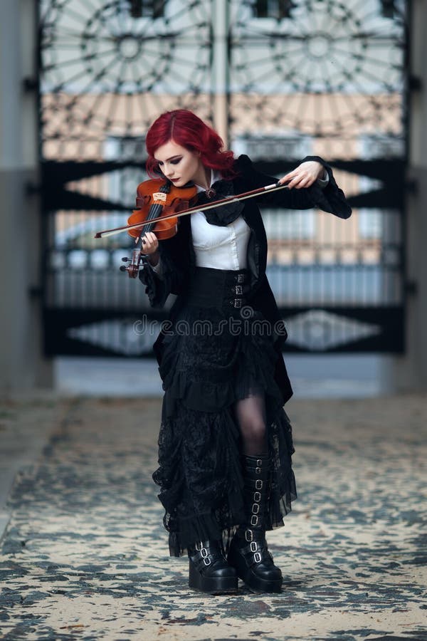 Red haired vampire girl plays the violin in an old Museum in Gothic black clothes and a tailcoat