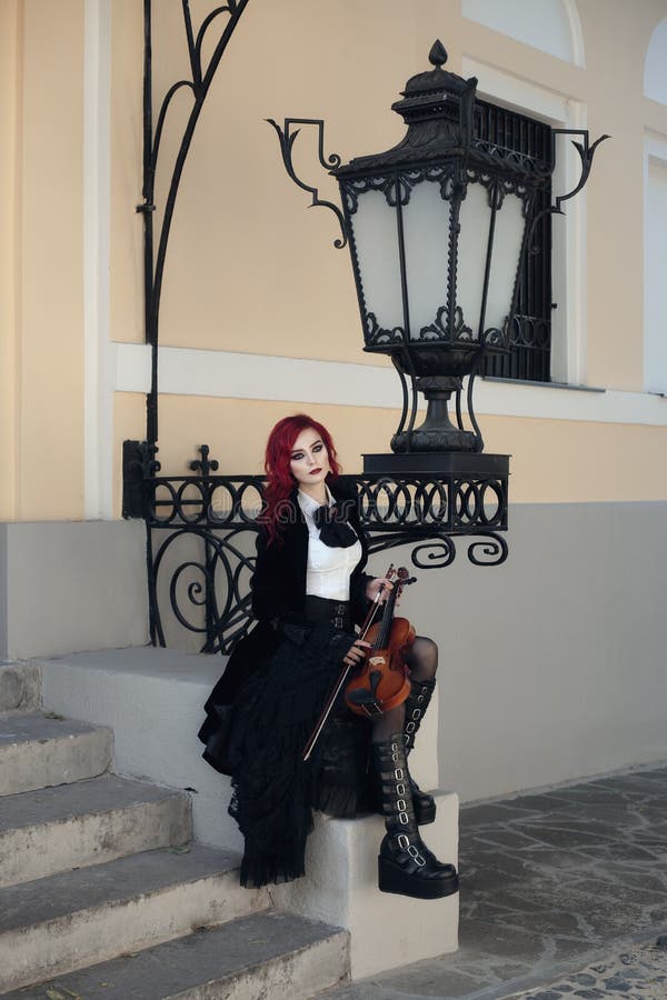 Red haired vampire girl plays the violin in an old Museum in Gothic black clothes and a tailcoat