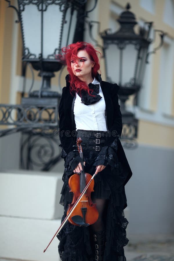 Red haired vampire girl plays the violin in an old Museum in Gothic black clothes and a tailcoat