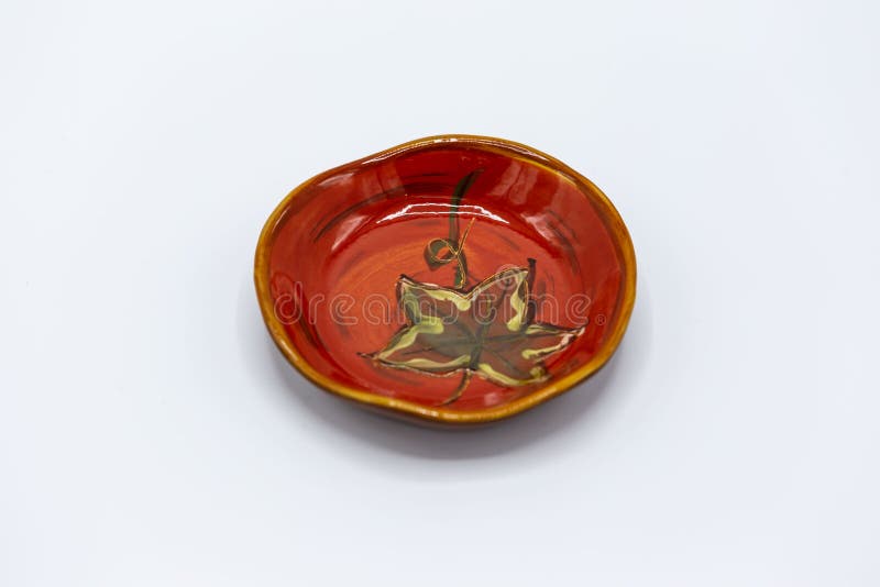 Red handmade small ceramic plate with a brown leaf on it