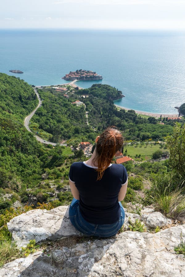 Red head girl hill enjoying Sveti Stefan island in Budva, Montenegro. Young woman looking to the adriatic sea and green cliff.