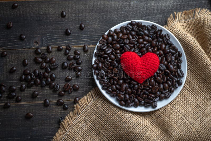 Red heart on a lot of roasted coffee beans background on white plate on wooden table. Strong black espresso, Grains of coffee back stock images Red heart on a lot of roasted coffee beans background on white plate on wooden table. Strong black espresso, Grains of coffee back stock images