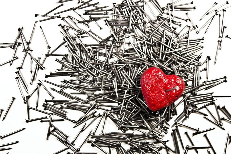 Red heart on pile of iron nails, pierced by a nail