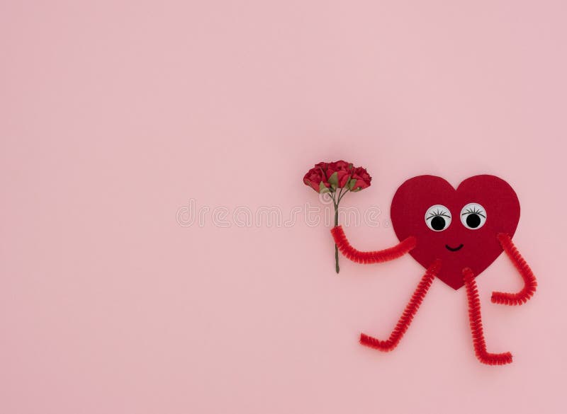 Red heart-shaped hero with small bouquet of craft red roses on pink background. Valentine greeting card. Valentine`s Day, love, happiness and wedding concept. Flat lay style with copy space