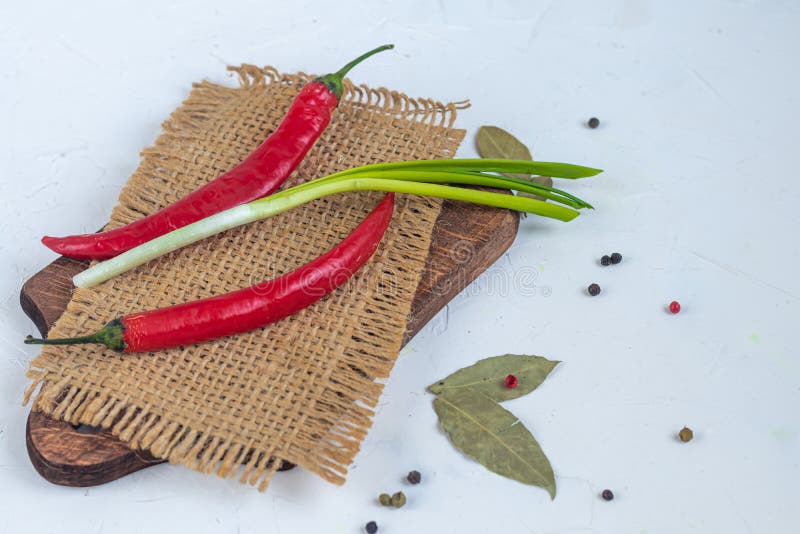 Red hot chili peppers on a wooden board. Near green onions, bay leaves, peppercorns. On white background royalty free stock images Red hot chili peppers on a wooden board. Near green onions, bay leaves, peppercorns. On white background royalty free stock images