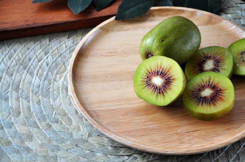 Pieces of Red Kiwifruit on Plate with Green Leaves on Background Stock