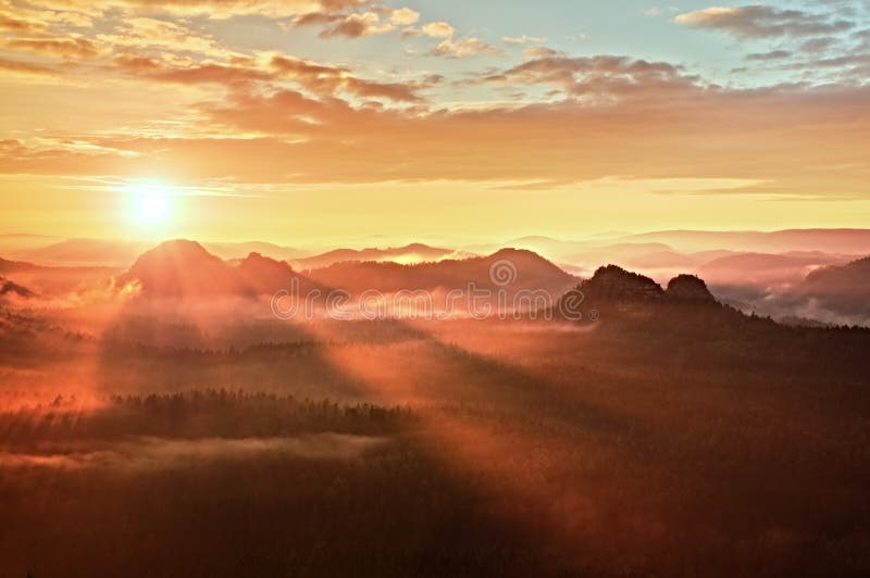 Red misty daybreak. Foggy autumn morning in a beautiful hills. Peaks of hills are sticking out from rich colorful clouds.