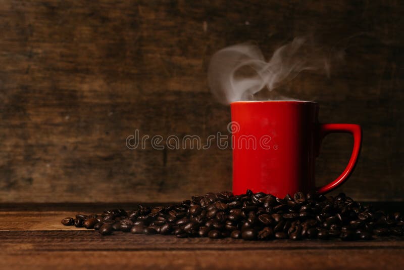 red mug with steam on a pile of fresh roasted coffee beans over wooden table