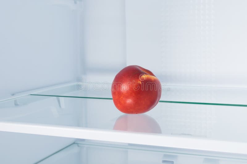 Red Nectarine Lies on a Shelf in an Empty Refrigerator Stock Photo