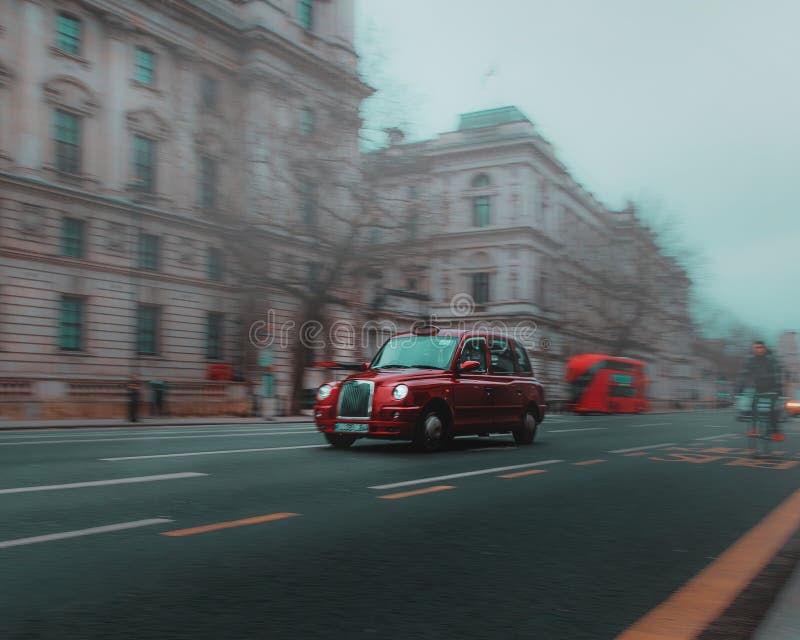 Red old traditional london taxi cab passing by, motion blurred with long exposure panning shot. Cold foggy winter day