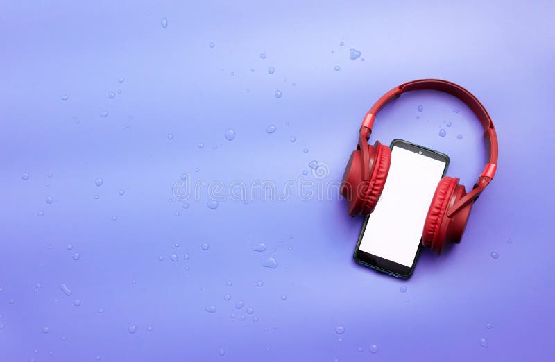 Red overhead music headphones with a smartphone with a white display copy space. Headphones with a gadget on a blue background in royalty free stock images