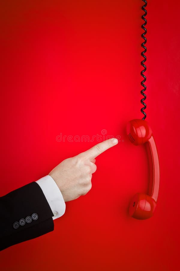 A man's index finger pointing at a red phone off of the hook and hanging by the cord. A man's index finger pointing at a red phone off of the hook and hanging by the cord.