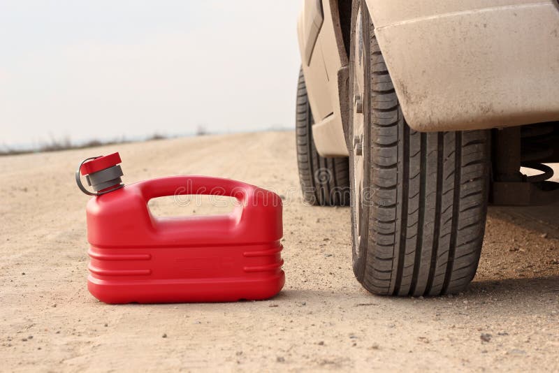 Red plastic fuel canister on dirt road with car