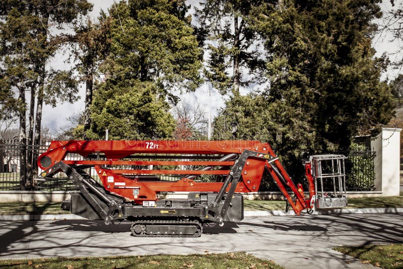 Red remote control tracked lift designed for tree work with basket parked in front of estate fence with evergreen trees,