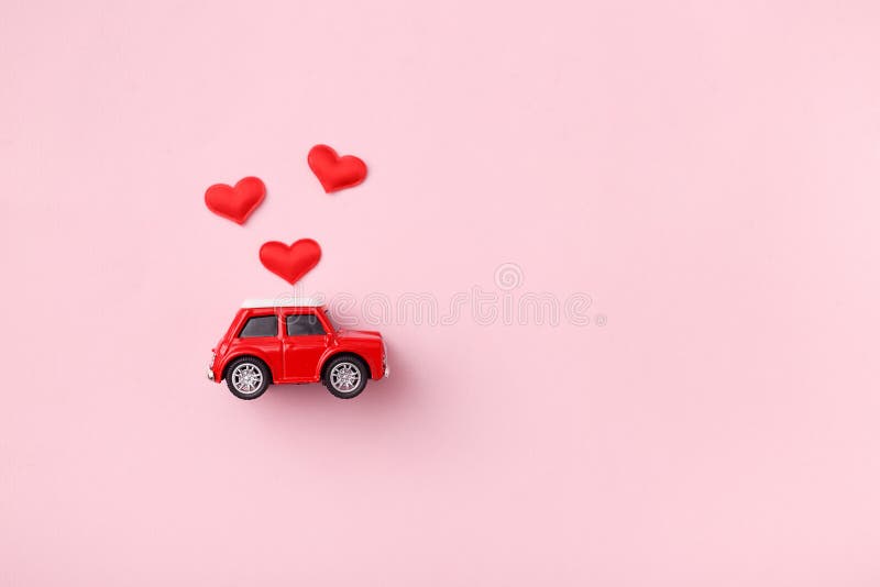 Red retro toy red car with red bow for Valentine`s day on pink background with heart confetti. Top view, flat lay