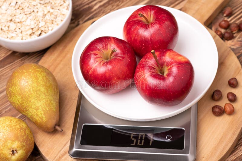 Red ripe apples on the kitchen scales on wooden table