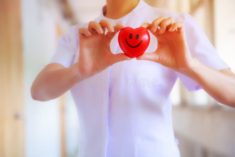 Red smiling heart held by female nurse`s hand, representing giving effort high quality service mind to patient. Professional, Spec