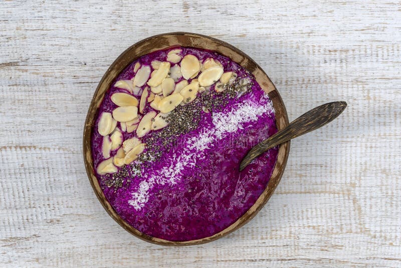 Red smoothie in coconut bowl with dragon fruit, avocado, almond flakes, coconut chips and chia seeds for breakfast , close up. The