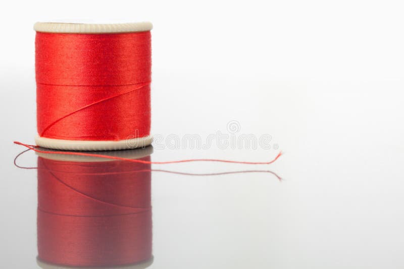 Red spool of thread on a table against a white background