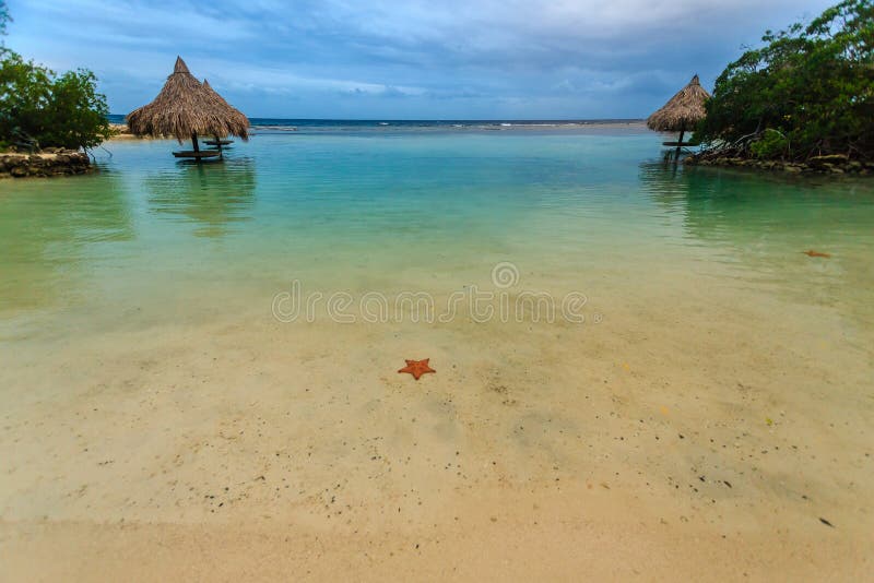 A red star fish washes onto the beach in a lovely tidal pool with tiki huts in a small cove at Little French Kay, Roatan, Honduras. A red star fish washes onto the beach in a lovely tidal pool with tiki huts in a small cove at Little French Kay, Roatan, Honduras
