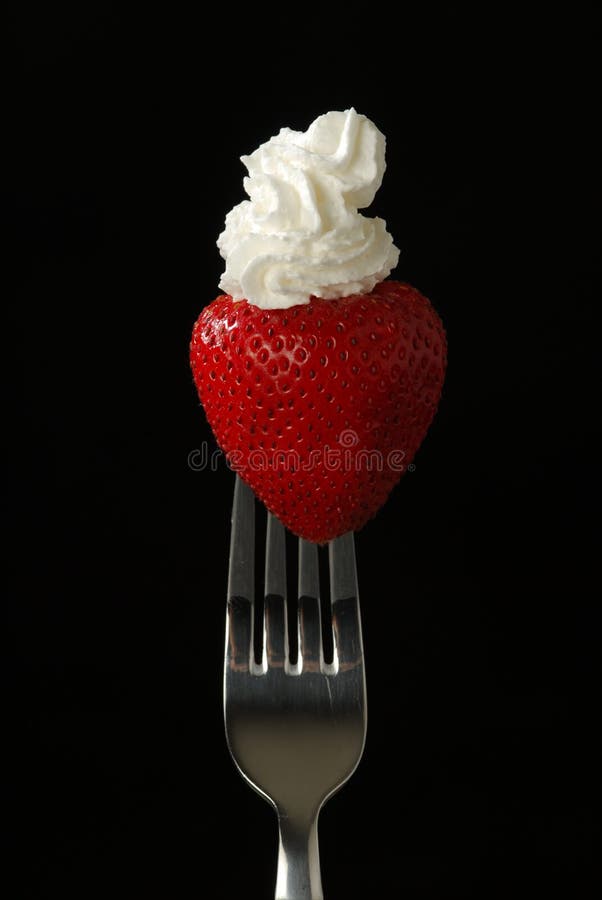 A fresh red strawberry on a fork with whipped cream and a black background