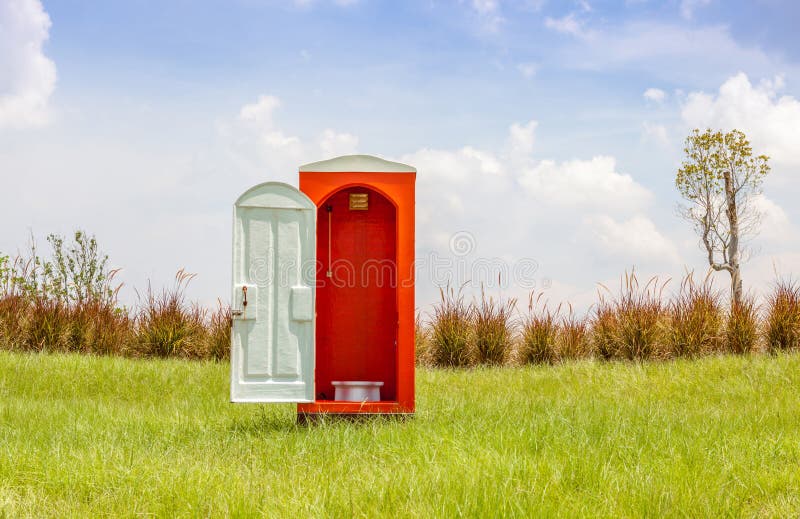 The red toilet with white door open contrast with green grass an