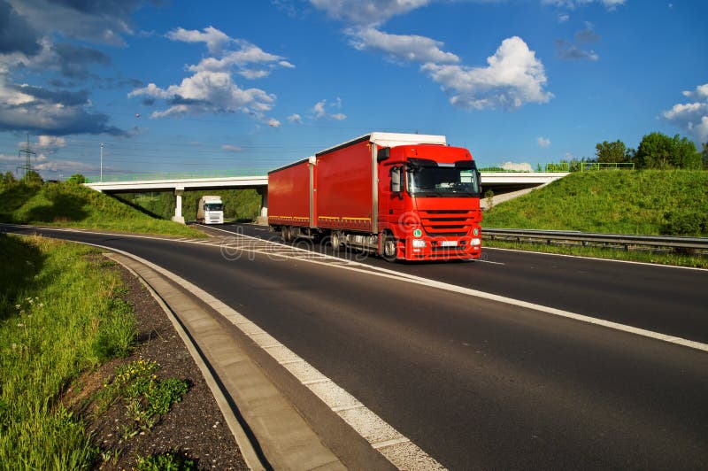 Red truck driving down the highway, under the bridge in the background goes white truck