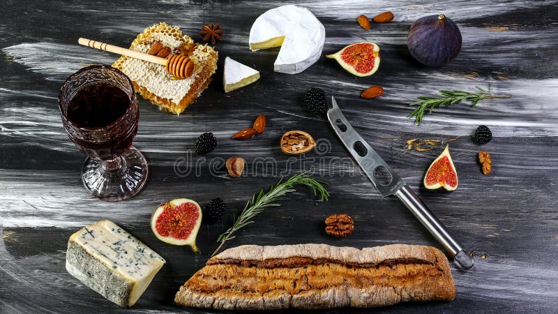 Red and white wine plus different kinds of cheeses cheeseboard on rustic wooden table. French food tasting party or feast scenery