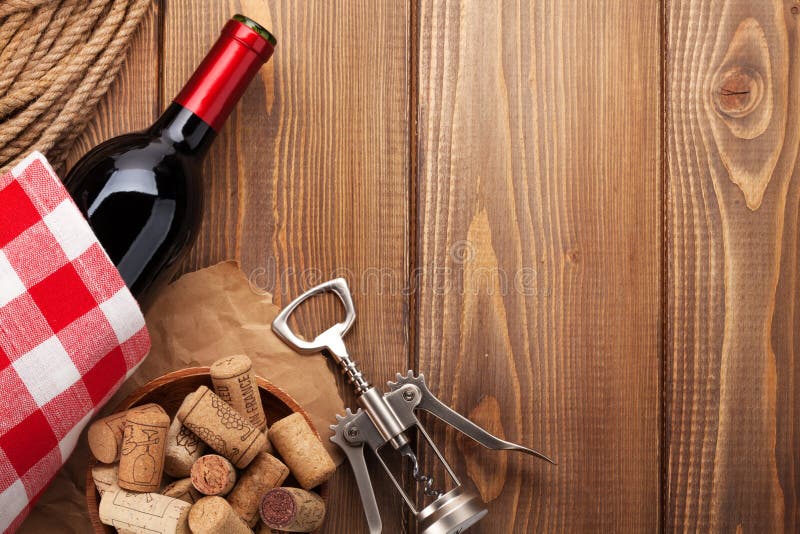 Red wine bottle, corks and corkscrew over wooden table backgroun