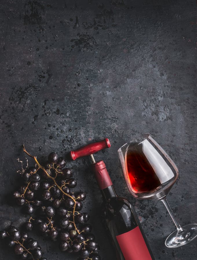 Red wine bottle with vintage corkscrew, glass and grapes on retro black background