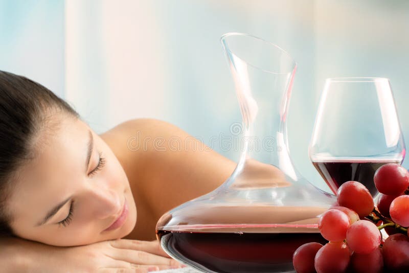 Red wine decanter and grapes with woman in background.