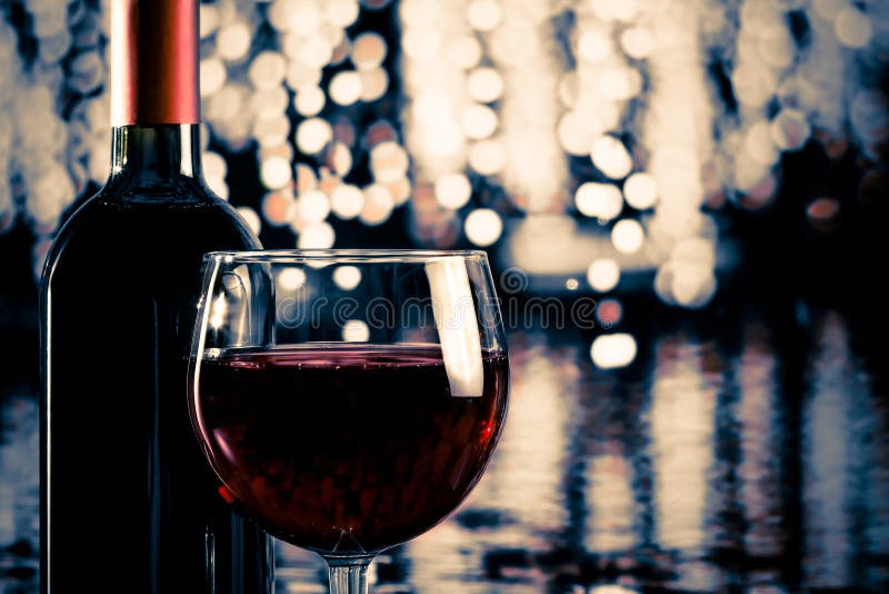 Red wine glass near bottle with light bokeh